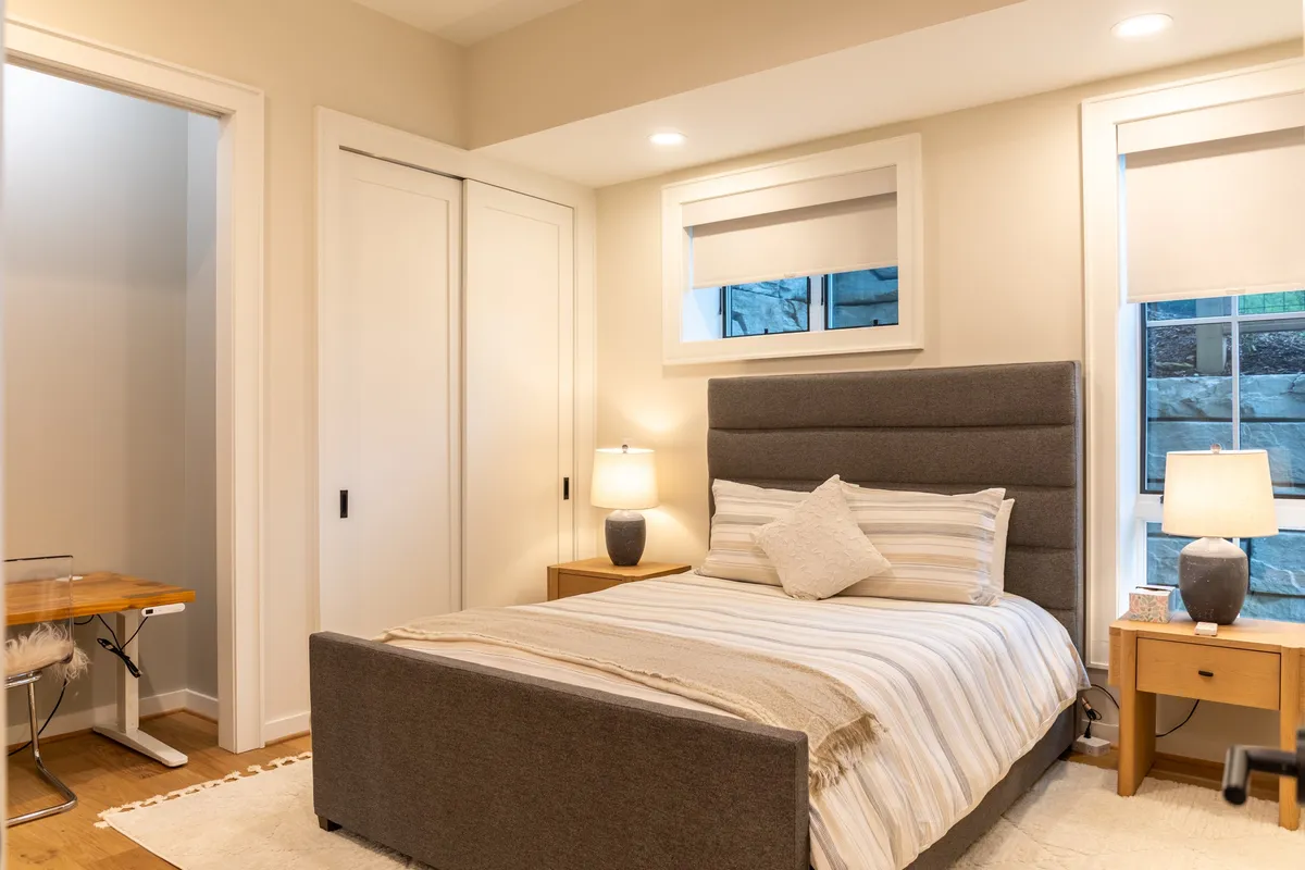 A serene queen bedroom with a plush upholstered bed, nightstands with lamps, and calm, neutral décor. The room offers a peaceful retreat, perfect for rest or remote work, embodying comfort and flexibility for guests.