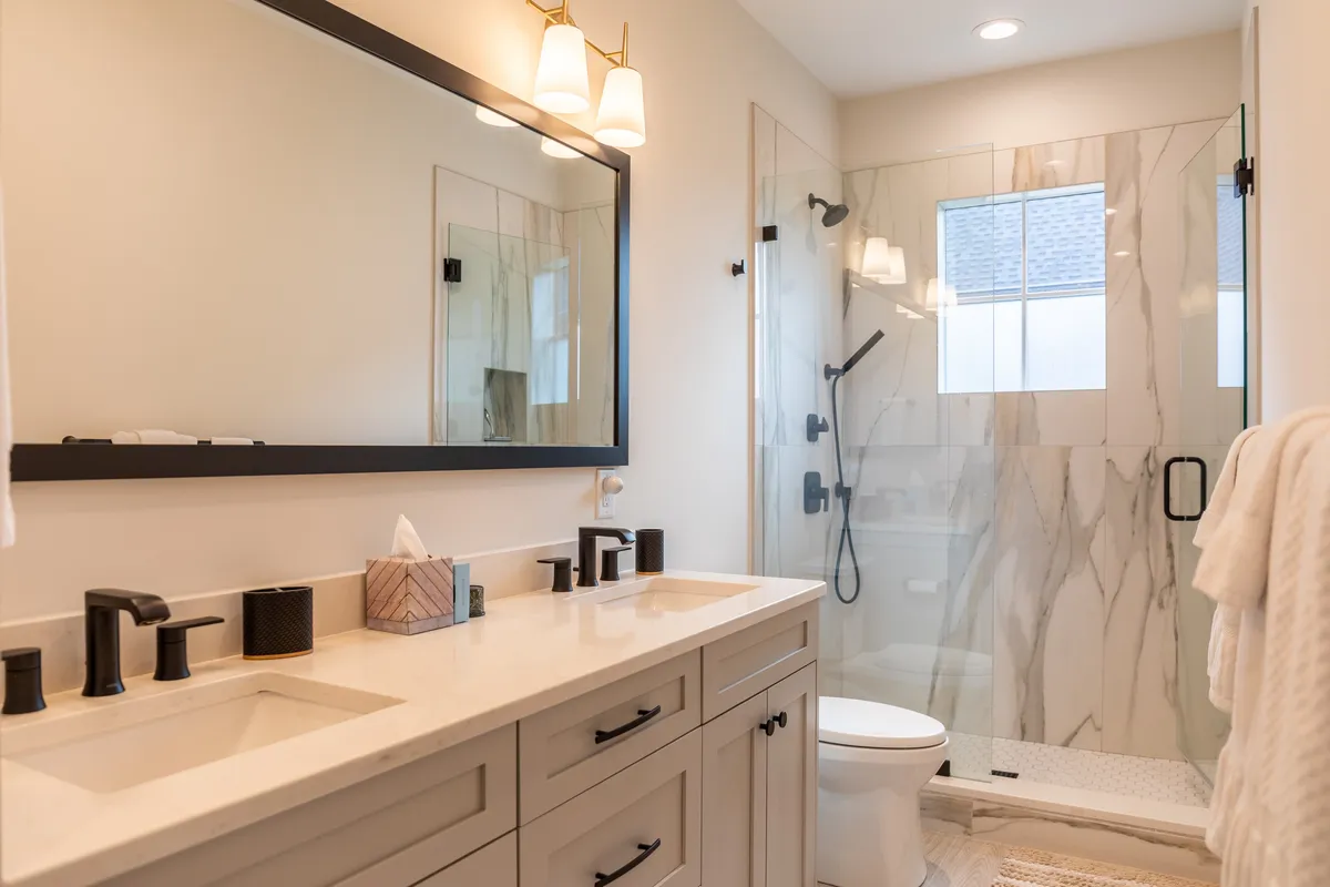 A modern, spa-inspired bathroom with a double vanity, large mirror, and a sleek glass shower enclosure. Decorative lighting fixtures add a touch of elegance, and the overall design radiates calm and indulgence.