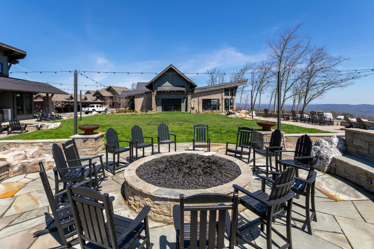 A welcoming outdoor fire pit surrounded by comfortable chairs, nestled on a manicured lawn with a community building in the background. The arrangement suggests a place for evening gatherings, storytelling, or stargazing after a day of adventure.