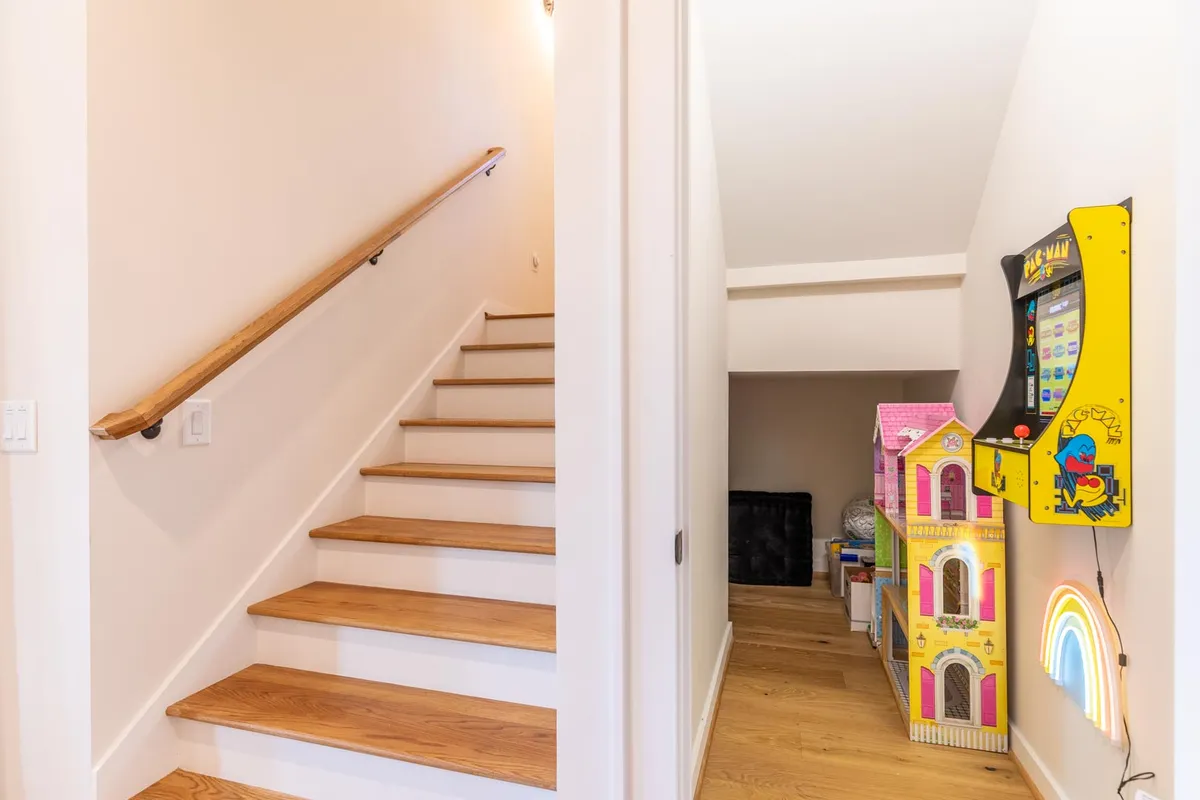 A cheerful play area with a visible staircase, arcade machine, and a scattering of toys, ideal for creative play and energetic game nights. The scene is lively and filled with possibilities for kids and families to interact and enjoy.