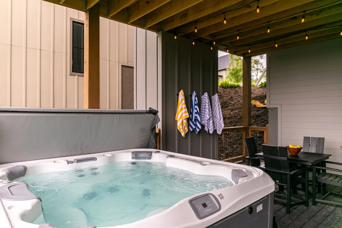 This image features an inviting outdoor hot tub area, complete with hanging towels and a nearby dining table. The setting is relaxed and social, ideal for unwinding after work or engaging in casual conversation with friends, all while being surrounded by nature.