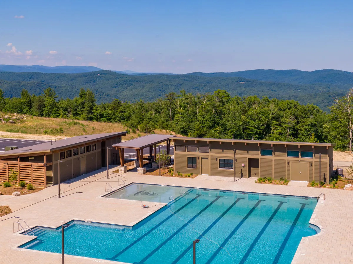 A vibrant exterior view of the Blue Ridge Mountain Club’s community pool set against a backdrop of lush mountains. The pool area features poolside cabanas and beautifully landscaped gardens, inviting families to swim, sunbathe, and relax in a scenic setting.